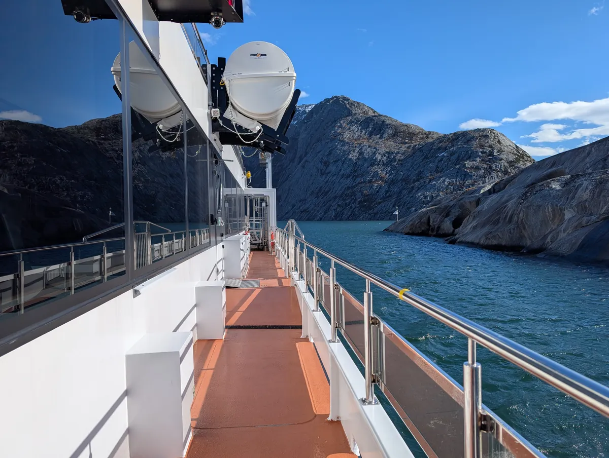 Pont latéral du Brim Explorer dans le passage du Saltstraumen, falaises rocheuses tout proches et eau calme sous un grand soleil.