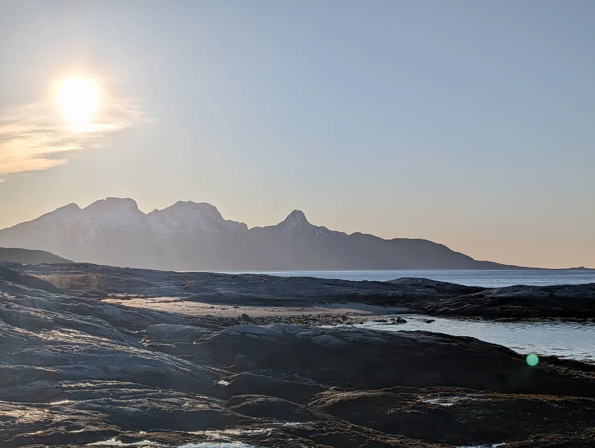 Fin d'après-midi sur la côte rocheuse au nord de Bodø, soleil bas et montagnes en silhouette de l'autre côté du fjord.