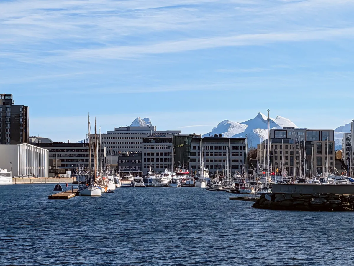 Vue depuis l'eau sur la marina, le centre-ville moderne de Bodø et les sommets enneigés du Børvasstindan en arrière-plan, par grand soleil.