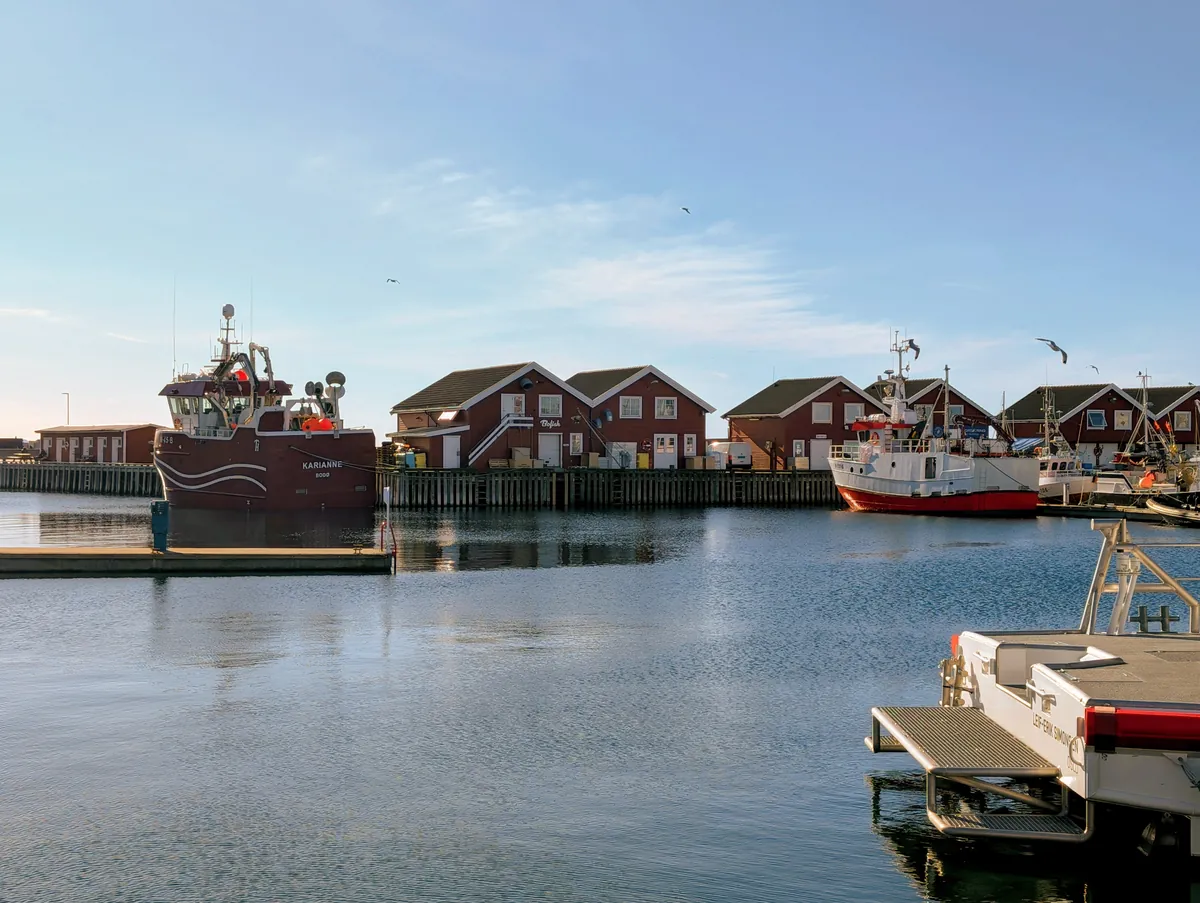 Le port de pêche de Bodø avec ses entrepôts rouges typiques (rorbu) et ses chalutiers à quai — ambiance norvégienne traditionnelle.