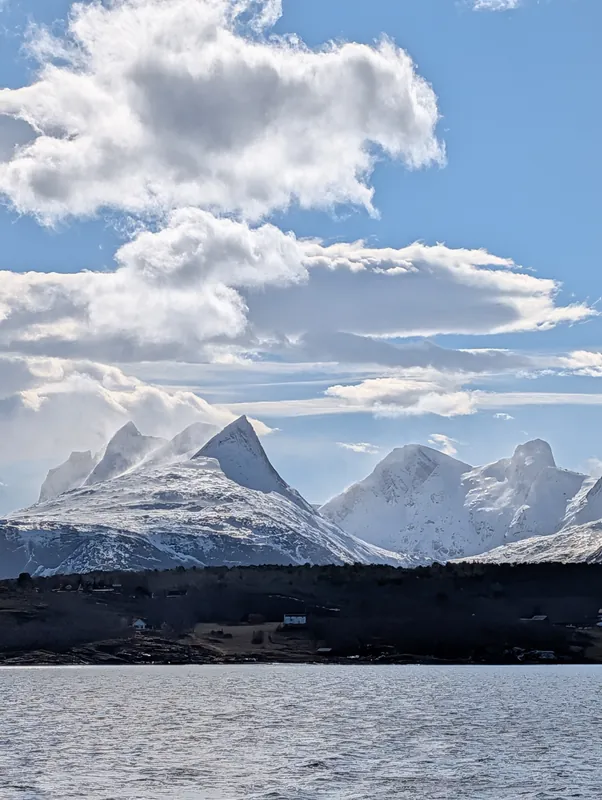 Vue spectaculaire depuis le bateau de Brim Explorer : un pic enneigé pointu se découpe dans des nuages dramatiques entre Bodø et Saltstraumen.