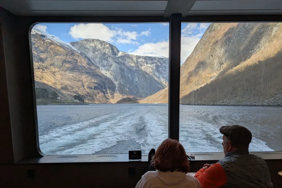 Passagers assis face à la baie vitrée arrière du catamaran avec vue sur le Naeroyfjord, croisière confortable.