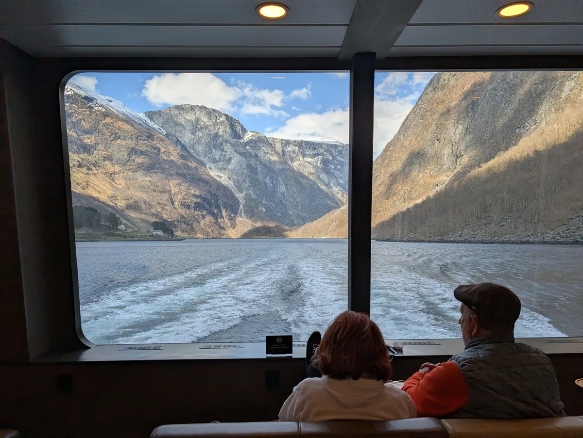 Passagers assis face à la baie vitrée arrière du catamaran avec vue sur le Naeroyfjord, croisière confortable.
