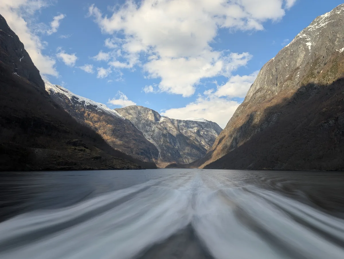 Pose longue saisissant le sillage du catamaran au cœur du Naeroyfjord, eau filée et falaises profondes, Norvège.