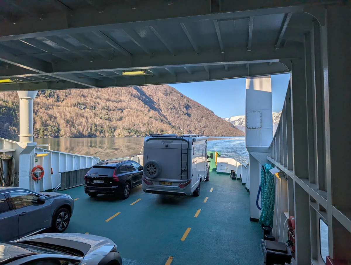 Pont voitures du ferry avec camping-cars et automobiles, ouverture latérale donnant sur les falaises ensoleillées du Geirangerfjord.