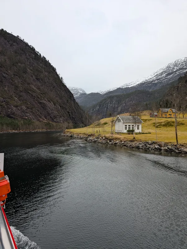 Maison blanche au bord du fjord, vue verticale Vue verticale d'une maison blanche traditionnelle au bord de l'Osterfjord, encadrée par des falaises et des montagnes enneigées, croisière Mostraumen.