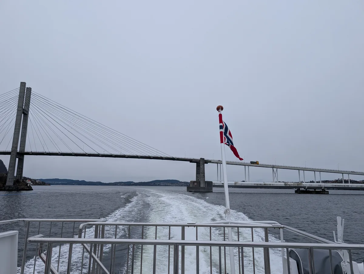 Pont de Nordhordland avec drapeau norvégien Passage sous le pont suspendu de Nordhordland depuis le pont arrière du bateau, drapeau norvégien au vent, lors de la croisière Mostraumen.
