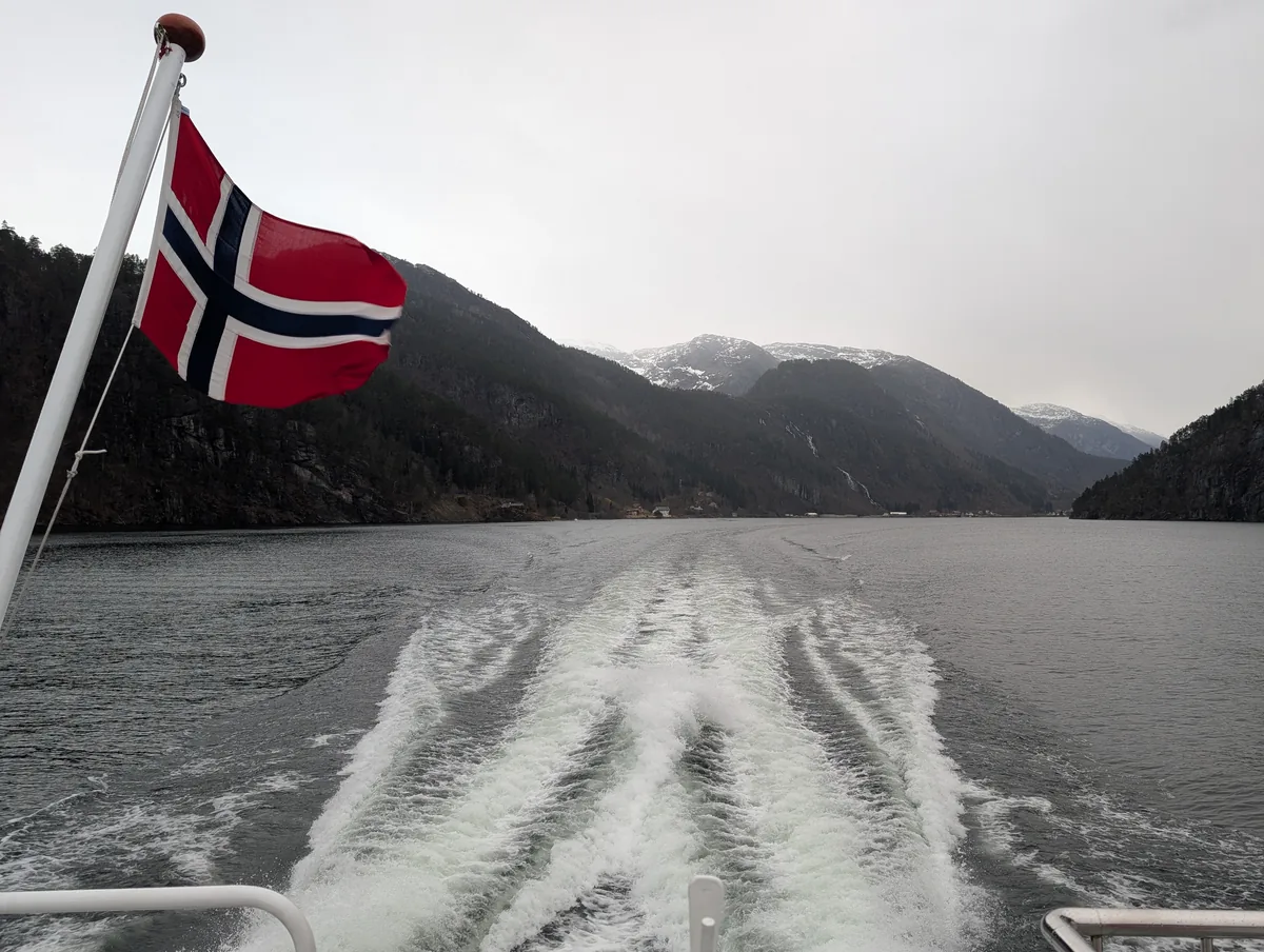 Sillage du bateau au retour avec drapeau norvégien Sillage du bateau de croisière dans l'osterfjord bergen au retour de Mostraumen vers Bergen, drapeau norvégien au vent et montagnes enneigées en arrière-plan.