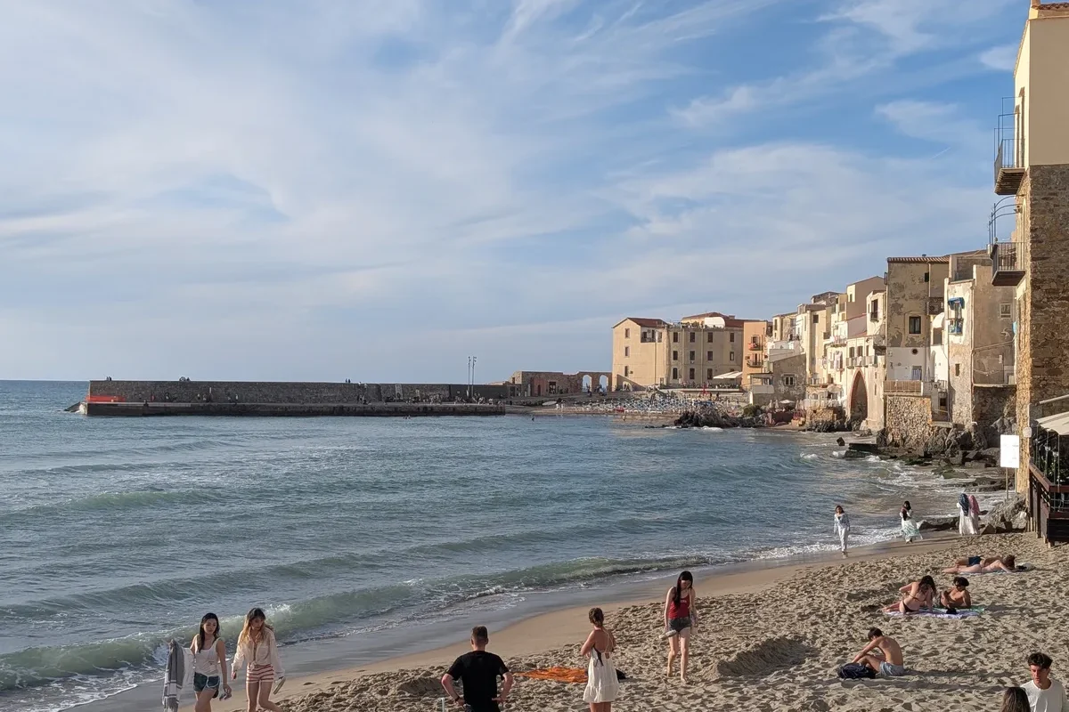 Vue panoramique de la plage de Cefalù en fin d'après-midi avec la vieille ville, le port et ses maisons colorées au bord de l'eau.