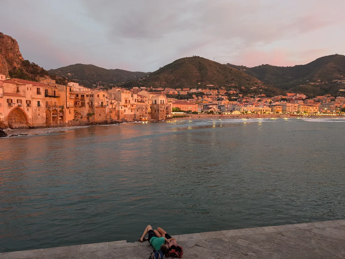 Vue depuis le quai au coucher de soleil, Cefalù Vue depuis le quai de Cefalù au coucher de soleil, avec la vieille ville baignée de lumière dorée et les montagnes verdoyantes.