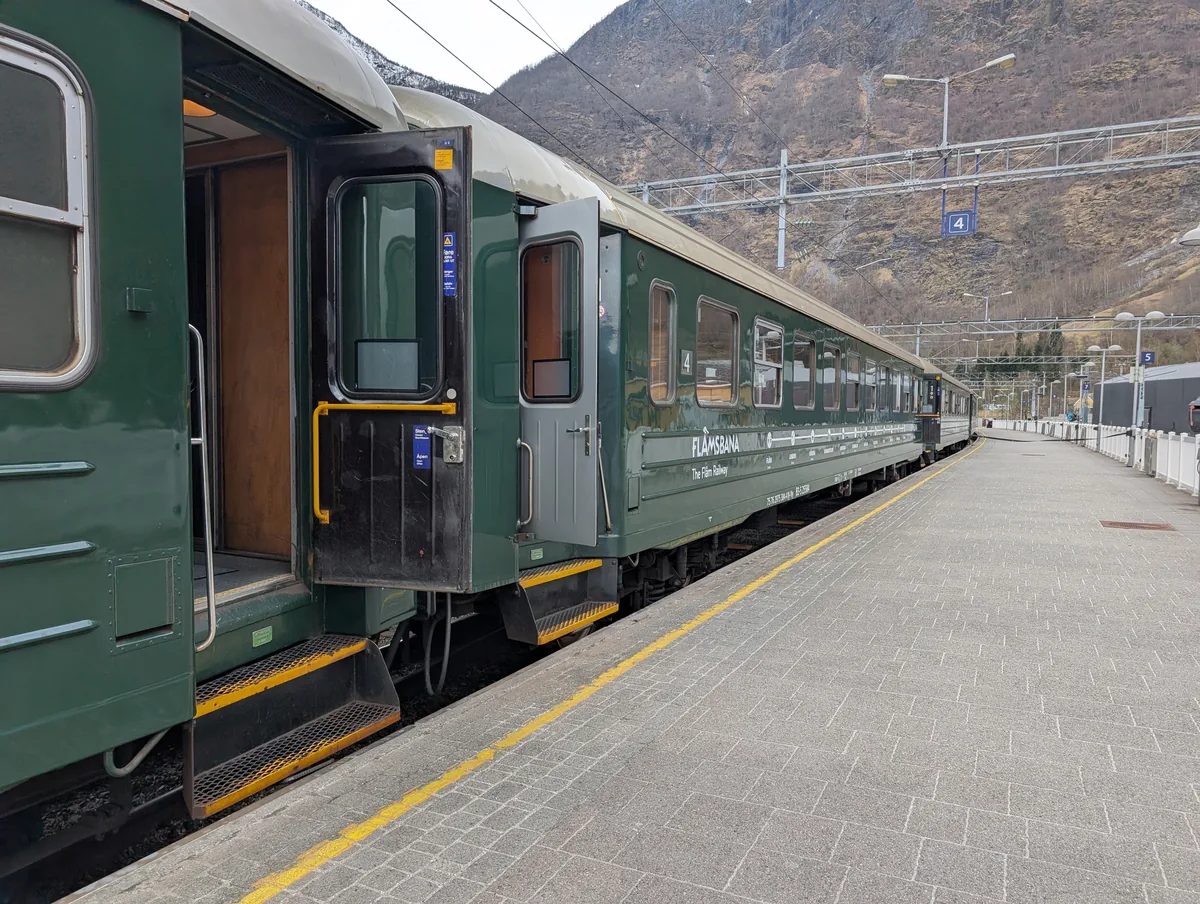 Train vert du Flåmsbana stationné à quai en gare de Flåm, portes ouvertes, avant le départ vers Myrdal en Norvège.