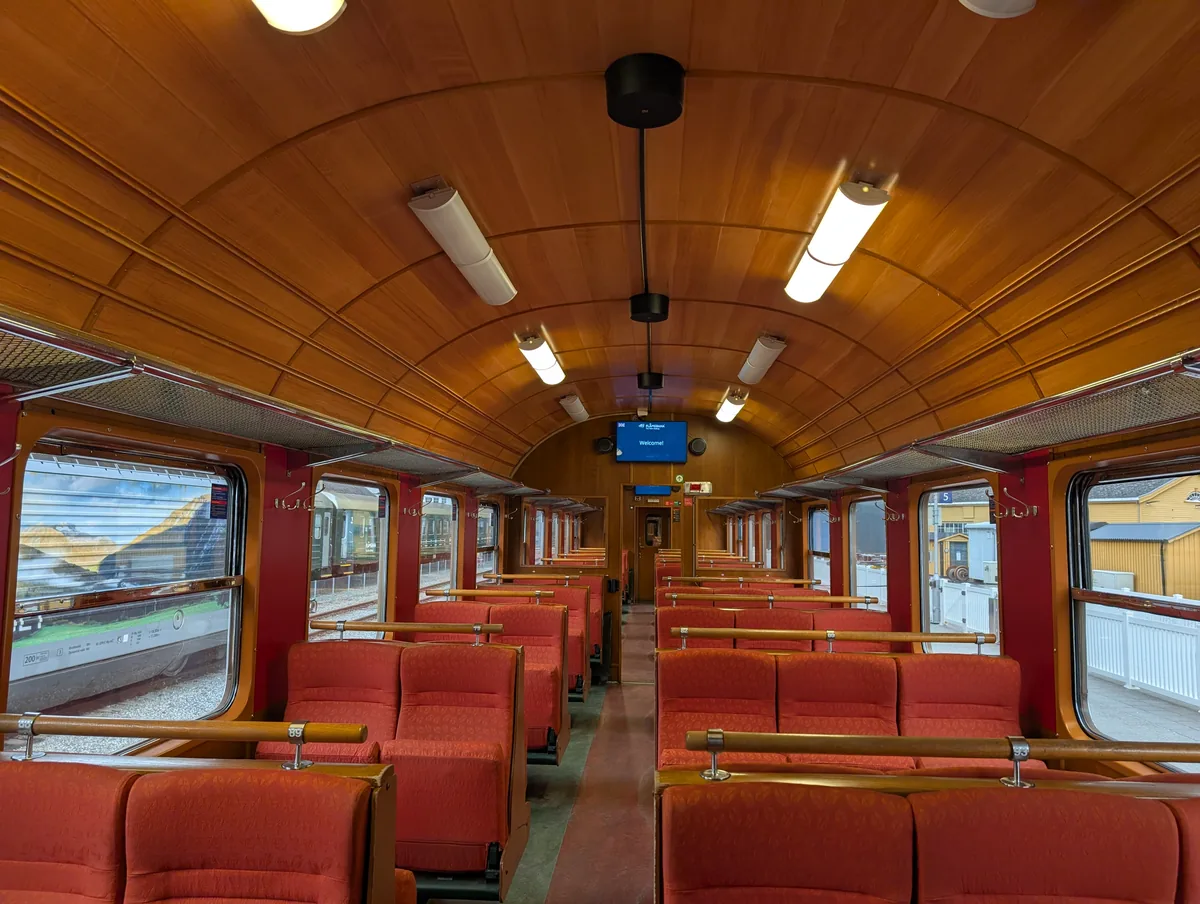 Intérieur boisé d'un wagon du train de Flåm avec ses banquettes rouges vides et son plafond en bois verni.
