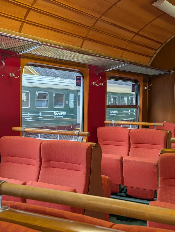 Banquettes rouges du train de Flåm le long des fenêtres, avec un autre wagon vert du Flåmsbana visible à l'extérieur.