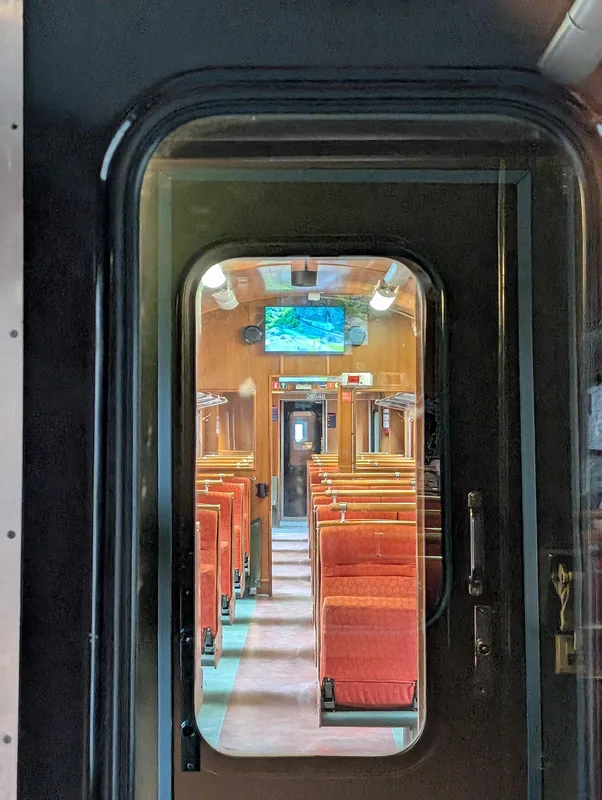 Vue à travers la vitre de la porte d'un wagon du train de Flåm sur les banquettes rouges de la voiture suivante.
