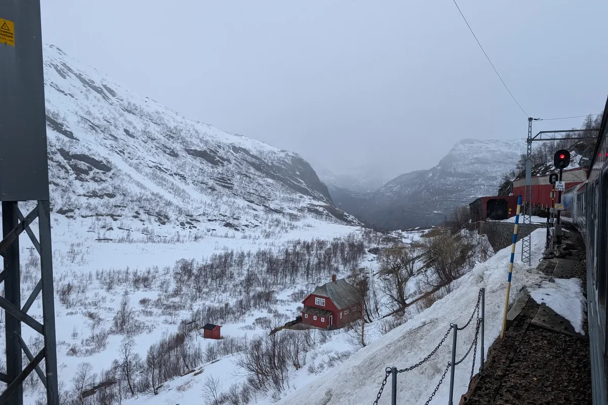Vallée entièrement enneigée avec une maison rouge isolée et la voie ferrée du train de Flåm approchant de Myrdal.