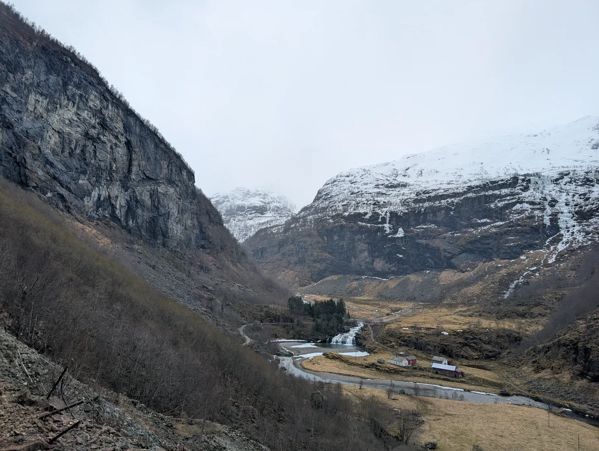 Vallée encaissée entre de hautes falaises avec une rivière et une maison rouge isolée, le long de la ligne du train de Flåm.