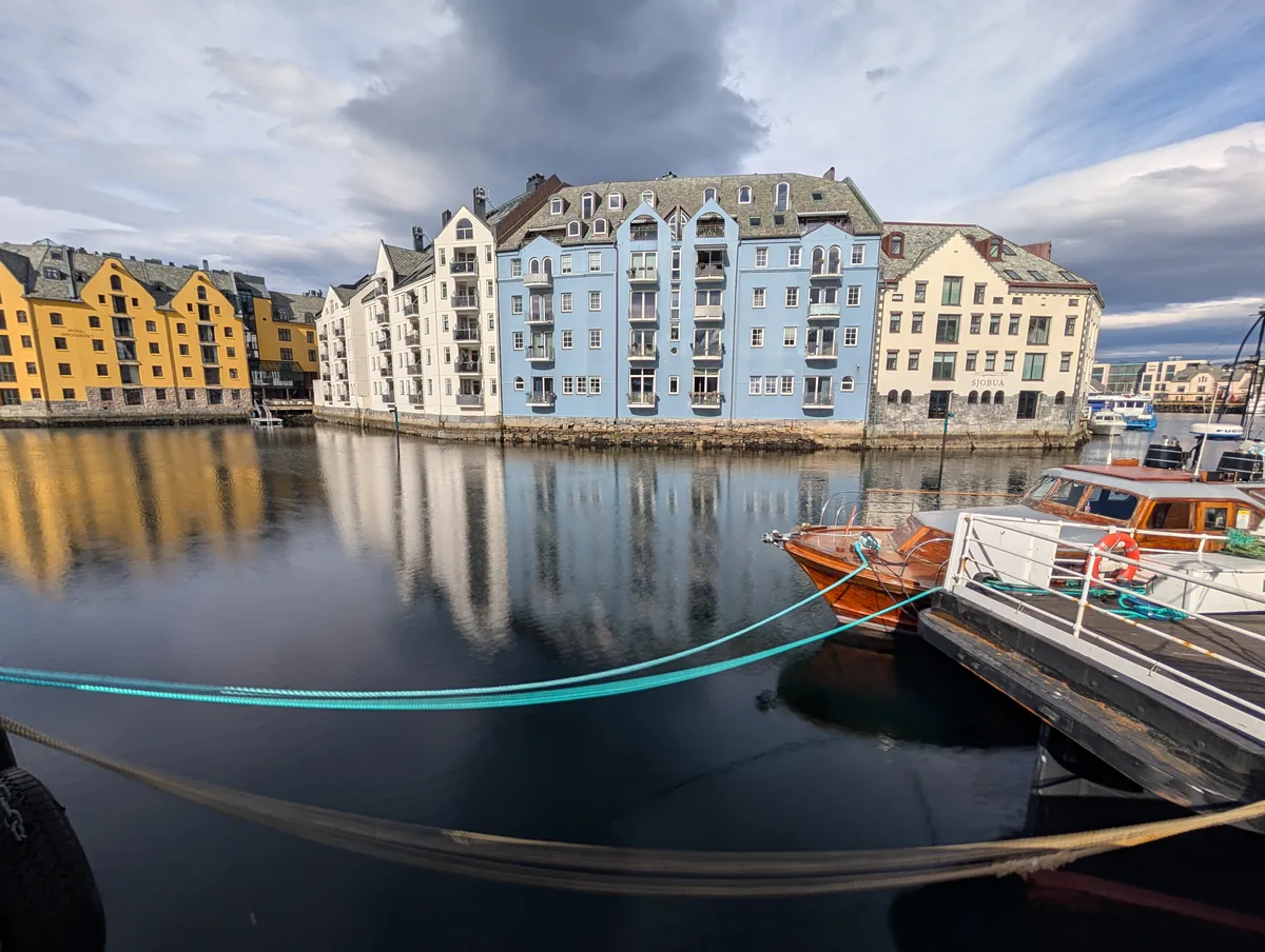 Canal Brosundet et maisons colorées d'Ålesund Canal Brosundet bordé de maisons Art nouveau bleues et jaunes se reflétant dans l'eau, avec des bateaux en bois à Ålesund.