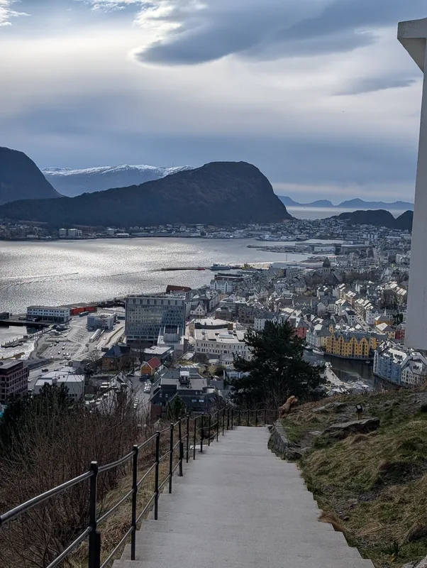 Montée du Mont Aksla et vue sur Ålesund Vue sur la ville d'Ålesund et le fjord depuis la montée du Mont Aksla, entre les arbres au-dessus des toits, en Norvège.