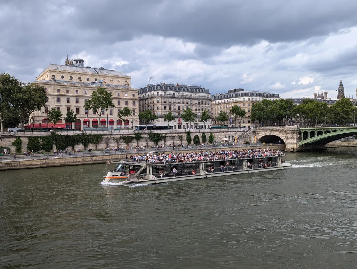 Bateau-mouche rempli de passagers longeant les quais de la Seine près du Châtelet, sous un ciel d'orage à Paris.