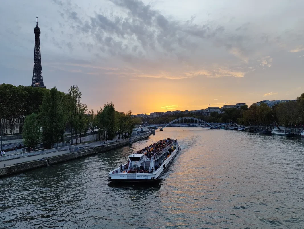Bateau-mouche remontant la Seine au coucher du soleil, avec la tour Eiffel et la passerelle Debilly en arrière-plan à Paris.