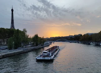 Faire une croisière sur la Seine à Paris – quel bateau choisir et pourquoi! Bateau-mouche remontant la Seine au coucher du soleil, avec la tour Eiffel et la passerelle Debilly en arrière-plan à Paris.