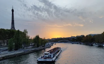 Faire une croisière sur la Seine à Paris – quel bateau choisir et pourquoi! Bateau-mouche remontant la Seine au coucher du soleil, avec la tour Eiffel et la passerelle Debilly en arrière-plan à Paris.