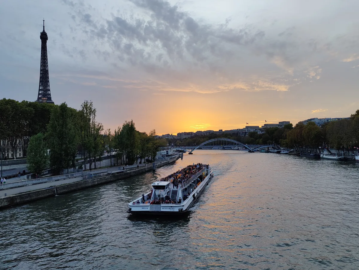 Bateau-mouche remontant la Seine au coucher du soleil, avec la tour Eiffel et la passerelle Debilly en arrière-plan à Paris.
