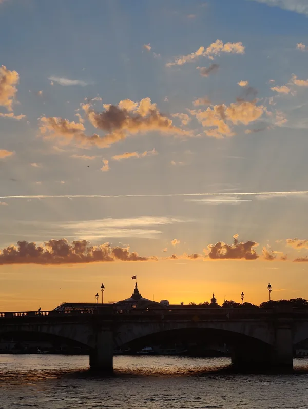 Coucher de soleil sur la Seine, avec la verrière du Grand Palais et un pont parisien en silhouette, vus depuis l'eau.