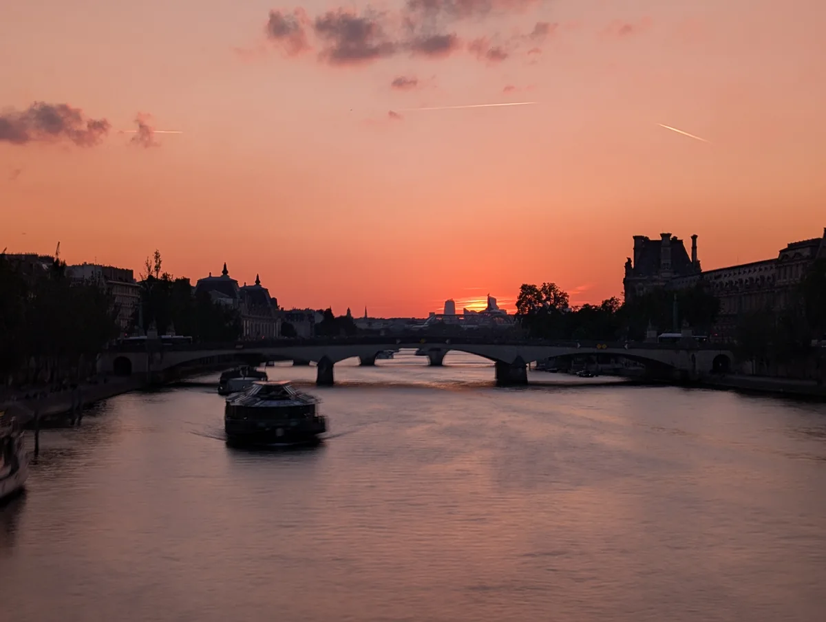 Pose longue d'un bateau de croisière sur la Seine au coucher du soleil, entre le Louvre à droite et le musée d'Orsay à gauche.