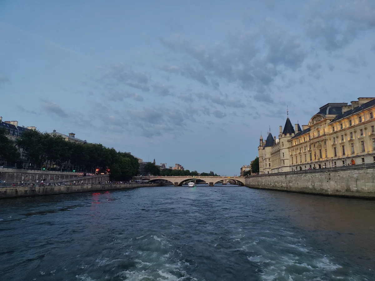 Sillage laissé par le bateau de croisière sur la Seine, avec la Conciergerie illuminée sur la droite et un pont parisien au fond.