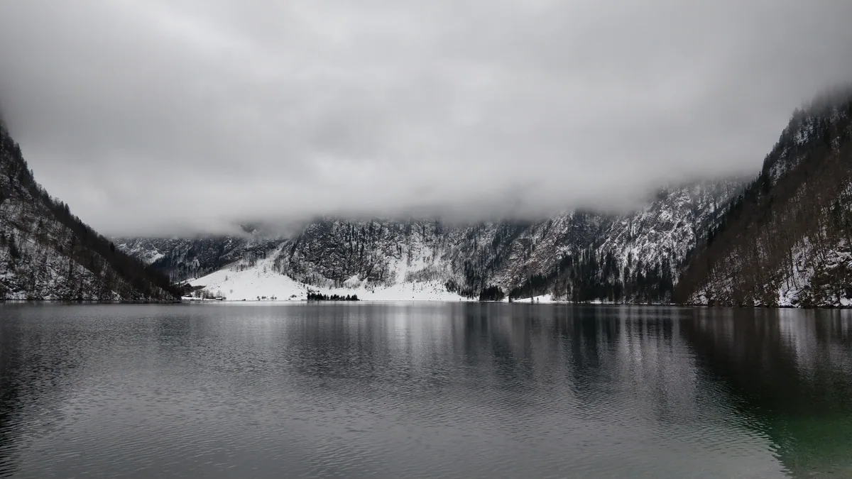 Le Königssee sous la neige en hiver Le Königssee en hiver, eau grise et montagnes couvertes de neige, sans le moindre bateau ni visiteur sur la rive.