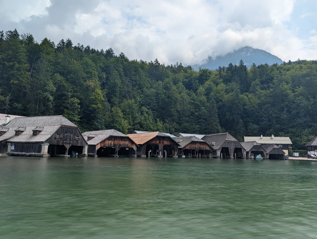 Les hangars à bateaux vus du Königssee Alignement de hangars à bateaux en bois au pied de la forêt, vus depuis le bateau sur le Königssee.