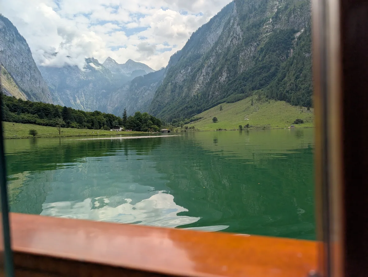 Le Königssee vu de la fenêtre du bateau Prairie et montagnes du Königssee encadrées par la fenêtre en bois verni d'un bateau électrique.