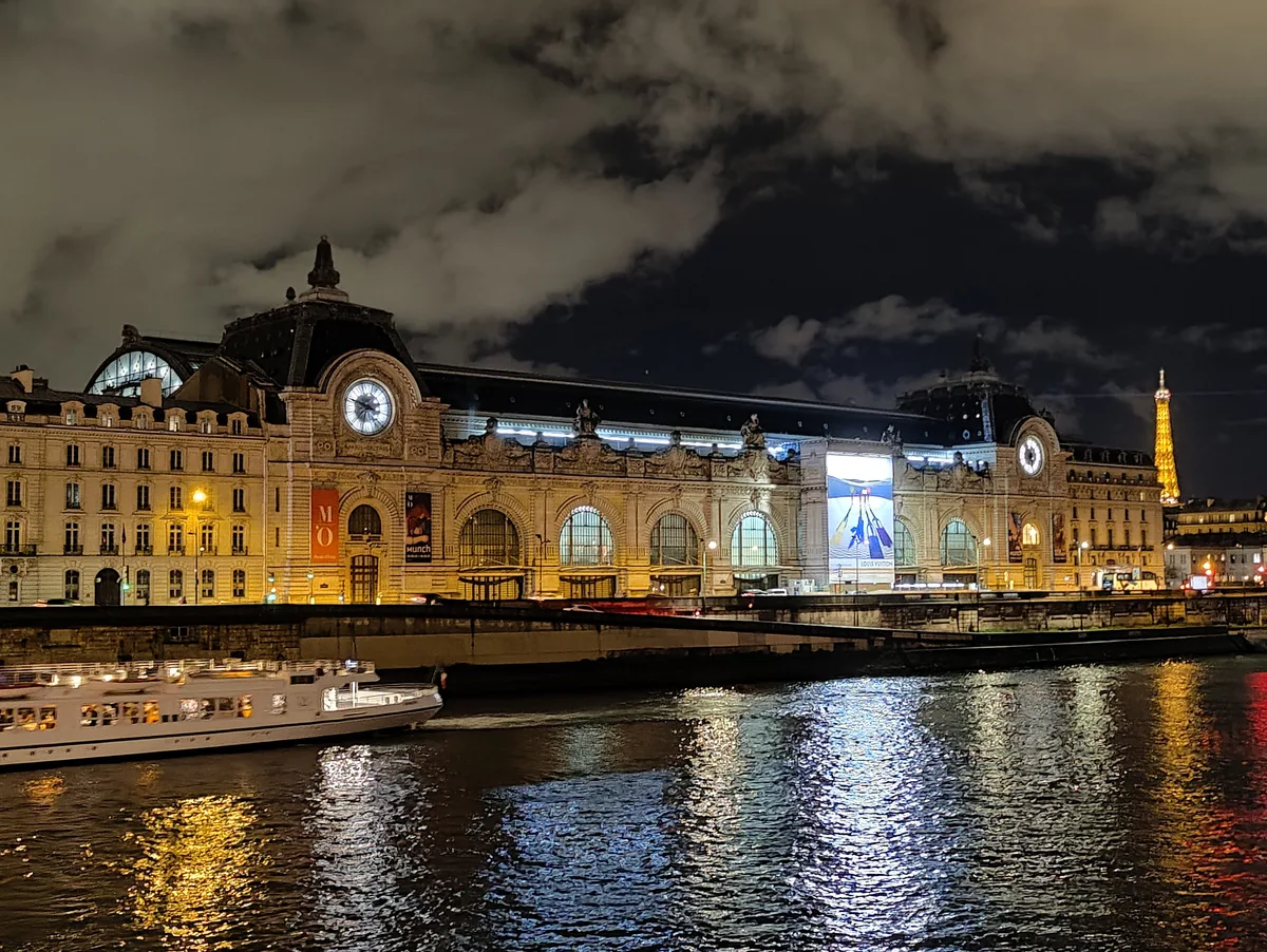 The Musée d'Orsay and the Seine by night in Paris The Musée d'Orsay lit up at night seen from the banks of the Seine, with the Eiffel Tower in the distance and reflections on the water in Paris.