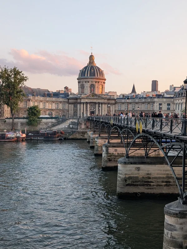 The Pont des Arts and the Institut de France The dome of the Institut de France at the end of the Pont des Arts at sunset, with strollers and the Seine in Paris.