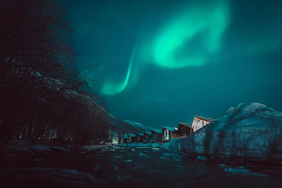 Aurores boréales vertes au-dessus des cabanes en bois du Tromsø Lodge & Camping en hiver, au bord de la rivière Tromsdalselva à cinq minutes du centre de Tromsø