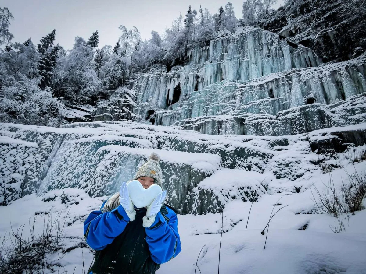 Frozen waterfalls in the Korouoma canyon in Finnish Lapland: walls of blue-tinged ice and giant icicles at the bottom of the snow-covered canyon, hikers at the foot of the frozen fall