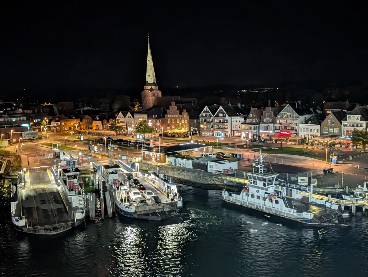 Die kleine Priwallfähre am Anleger vor den beleuchteten Häusern von Travemünde, nachts von der TT-Line-Fähre nach Trelleborg gesehen