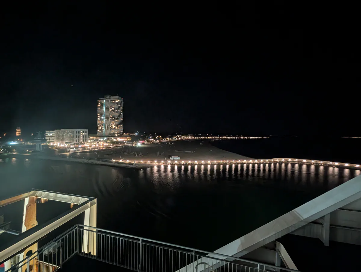 Der Strand von Travemünde und das beleuchtete Maritim-Hochhaus bei Nacht, von der Fähre aus gesehen, die in die Ostsee hinausfährt