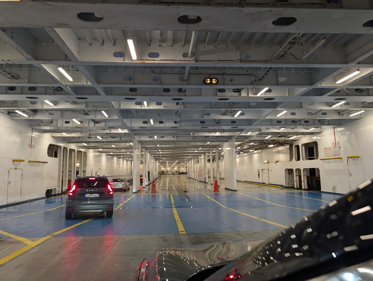 Autos parken auf dem blau-weißen Autodeck der TT-Line-Fähre, geleitet von den gelben Linien vor der Abfahrt