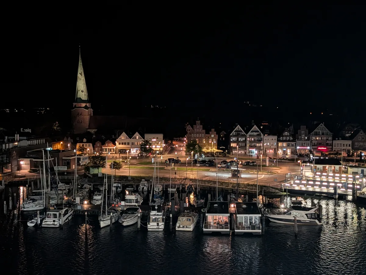 Uferpromenade von Travemünde bei Nacht mit Kirchturm, Giebelhäusern und Yachthafen, von der Fähre aus gesehen