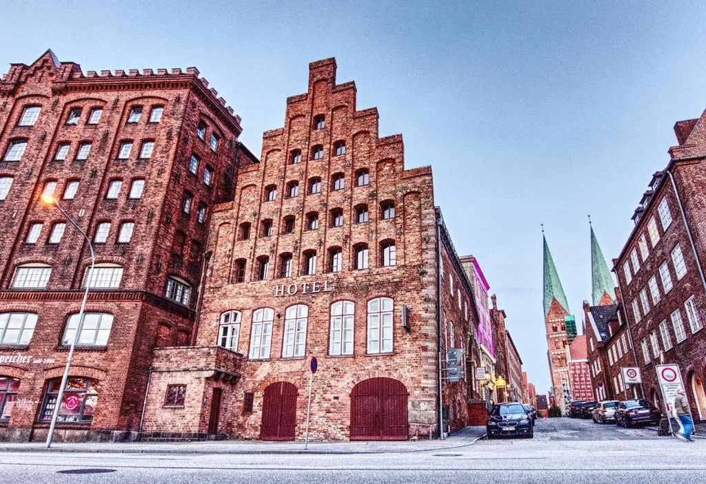 Rote Backsteinfassade mit Giebel des Hotel Anno 1216 in der Lübecker Altstadt, im Hintergrund die Türme der Marienkirche