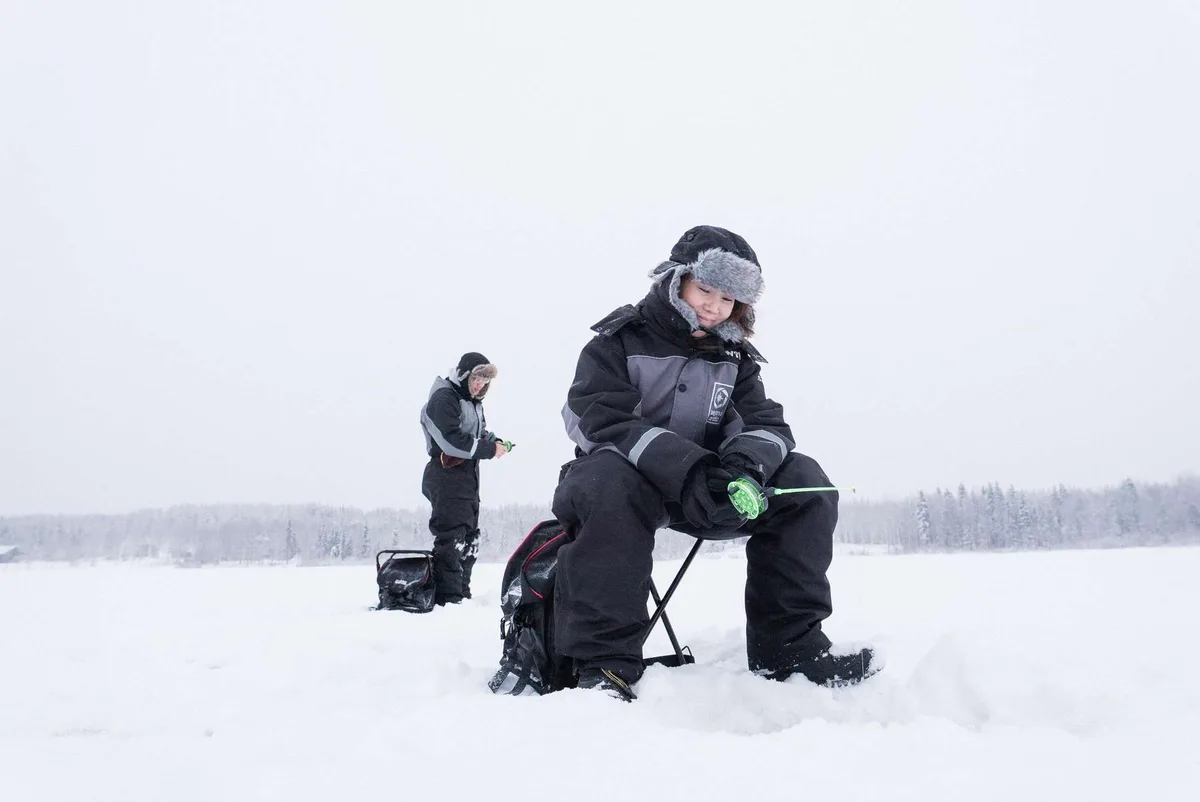 Ice fishing near Rovaniemi with Beyond Arctic: a hole drilled through a metre of ice on a frozen Lapland lake, campfire in a traditional kota and snowy winter landscape