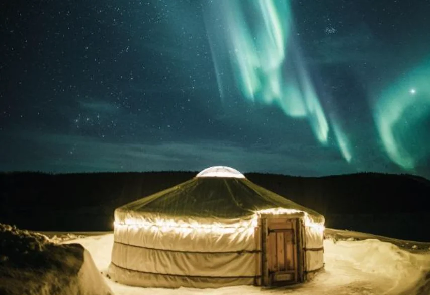 Yourte illuminée du Yurt District sous une aurore boréale verte, dans la neige près de Rovaniemi en Laponie finlandaise